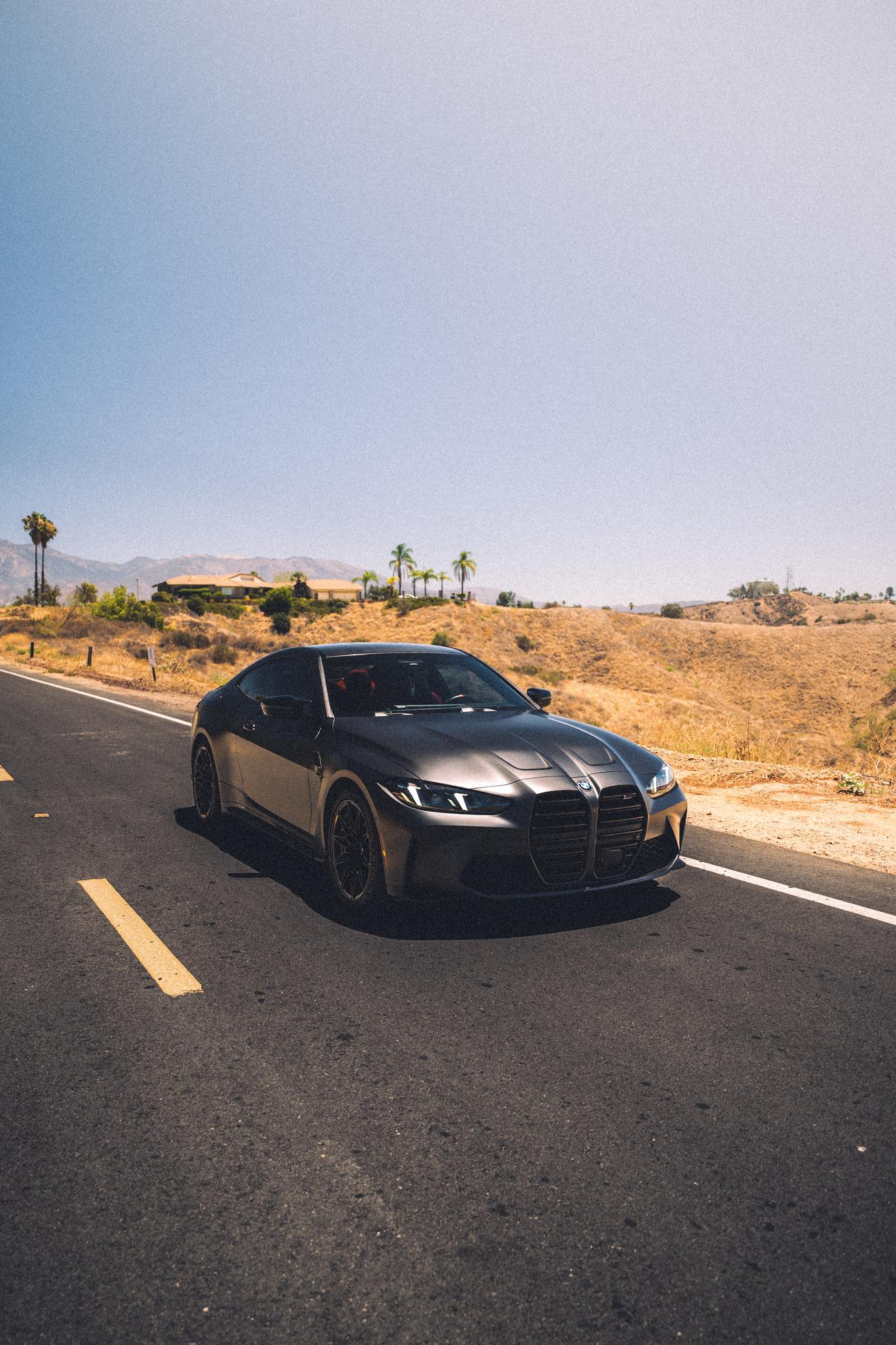 Three-quarter front view of the tinted matte gray BMW M4 against dry golden hills